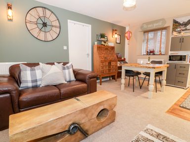 A living room with a brown leather sofa and wooden coffee table next to a dining table and chairs at Cwm Caeth Cottage in Nantmor near Beddgelert