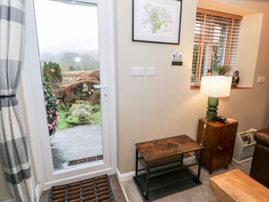 A door with a view of a garden next to a small table and a lamp on a cabinet at Cwm Caeth Cottage in Nantmor near Beddgelert
