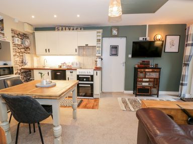 A kitchen and dining area with wooden table and chairs a wall mounted TV and a cabinet at Cwm Caeth Cottage in Nantmor near Beddgelert