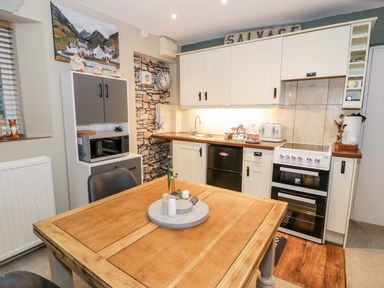 A kitchen with a wooden table and black chairs a microwave oven cabinets and a stove at Cwm Caeth Cottage in Nantmor near Beddgelert
