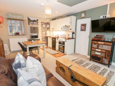 A kitchen and living room with a dining table and chairs a sofa with pillows and a wall-mounted tv at Cwm Caeth Cottage in Nantmor near Beddgelert