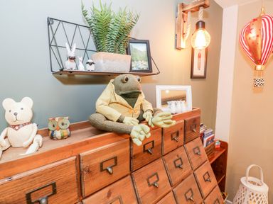 A wooden cabinet with drawers holding a frog doll, a teddy bear figurine, an owl figurine and other decorations at Cwm Caeth Cottage in Nantmor near Beddgelert