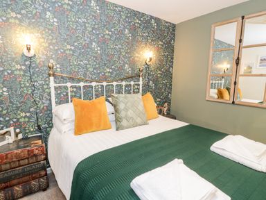 A bedroom with a bed with pillows and a green throw blanket and floral wallpaper at Cwm Caeth Cottage in Nantmor near Beddgelert