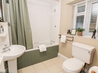 A bathroom with a bathtub and shower curtain a sink a toilet and a window with white blinds at Cwm Caeth Cottage in Nantmor near Beddgelert