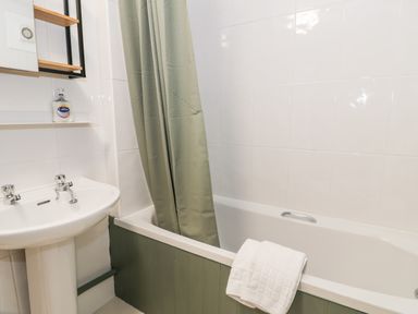 A bathroom with a bathtub a green shower curtain a white towel on the tub and a sink with a bottle of hand soap at Cwm Caeth Cottage in Nantmor near Beddgelert