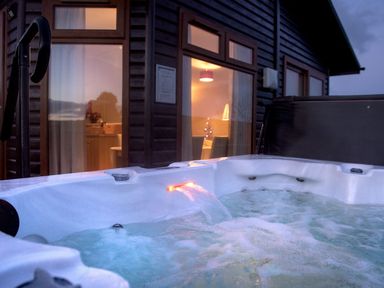 An outdoor hot tub with water jets in front of a wooden cabin with large windows at Chi Prenn Byhan in Tintagel