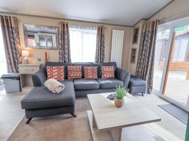 A living room with a gray sectional sofa and patterned cushions a wooden coffee table and large windows at Windermere View in Pony Meadow 37 White Cross Bay near Windermere