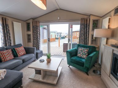 A living room with two sofas a coffee table and a floor lamp by sliding glass doors at Windermere View in Pony Meadow 37 White Cross Bay near Windermere