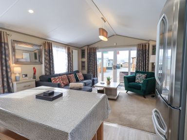 A living room with a dining table sofa armchair coffee table and large glass doors at Windermere View Pony Meadow 37 White Cross Bay near Windermere