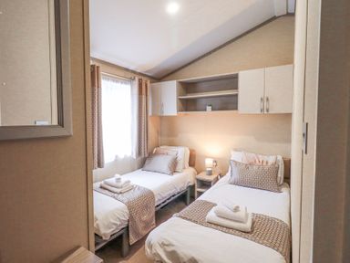 A bedroom with two single beds side by side a nightstand with a lamp between them and wall cabinets above at Windermere View in Pony Meadow 37 White Cross Bay near Windermere