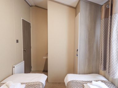A bedroom with two single beds a wardrobe a door and a radiator at Windermere View in Pony Meadow 37 White Cross Bay near Windermere
