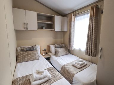 A bedroom with two single beds side by side with towels on each bed and a window with curtains at Windermere View Pony Meadow 37 White Cross Bay near Windermere