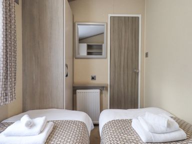 A bedroom with two single beds with folded towels a wardrobe a wall mirror and a wooden door at Windermere View in Pony Meadow 37 White Cross Bay near Windermere