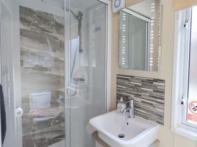 A bathroom with a shower cubicle a toilet a sink with soap a mirror with lights and a window at Windermere View in Pony Meadow 37 White Cross Bay near Windermere
