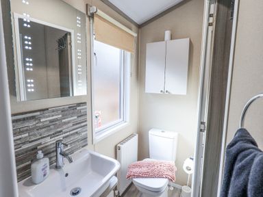 A bathroom with a sink a mirror a toilet a wall cabinet and a window at Windermere View in Pony Meadow 37 White Cross Bay near Windermere