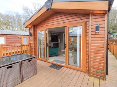 A wooden cabin with sliding glass doors opening to a deck with rattan storage boxes at Windermere View in Pony Meadow 37 White Cross Bay near Windermere