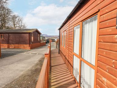 A wooden pathway beside caravan homes with hills and trees in the background at Windermere View Pony Meadow 37 White Cross Bay near Windermere