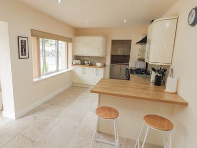 A kitchen with wooden countertops, bar stools, and a window with blinds at Awel Y Berwyn in Llangynog