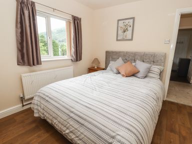 A bedroom with a bed striped bedding pillows a bedside table lamp window with curtains and a framed floral picture at Awel Y Berwyn in Llangynog