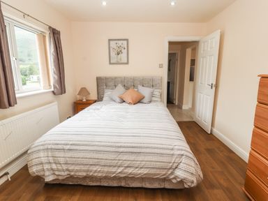 A bedroom with a bed bedside table lamp window and chest of drawers at Awel Y Berwyn in Llangynog