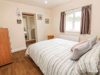 A bedroom with a bed pillows wooden chest of drawers window with curtains and framed pictures on the wall at Awel Y Berwyn in Llangynog