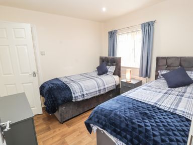 A bedroom with two single beds a nightstand with a lamp and a window with blue curtains at Awel Y Berwyn in Llangynog
