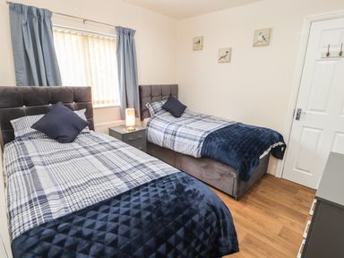 A bedroom with two single beds a bedside table with a lamp a window with curtains and wall art at Awel Y Berwyn in Llangynog