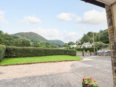 A driveway with gravel and concrete surrounded by hedges with a view of hills and houses at Awel Y Berwyn in Llangynog