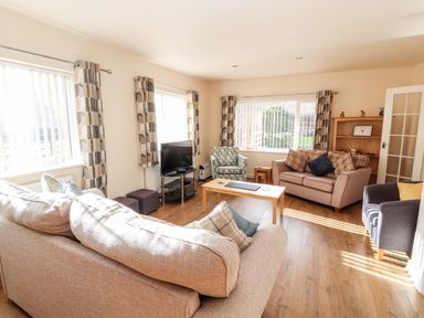 A living room with sofas armchairs a coffee table a television and windows with patterned curtains at Awel Y Berwyn in Llangynog
