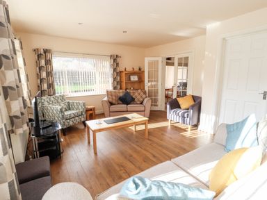 A living room with multiple chairs a sofa a coffee table a television and large window at Awel Y Berwyn in Llangynog