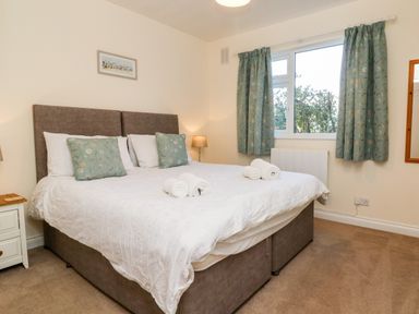 A bedroom with a large bed with pillows and rolled towels beside a window with curtains at Stonewood Lodge in Woolsery