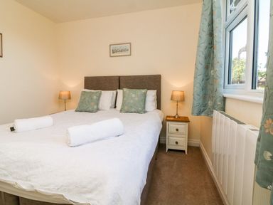 A bedroom with a bed with white bedding and rolled towels two bedside tables with lamps and a window with curtains at Stonewood Lodge in Woolsery