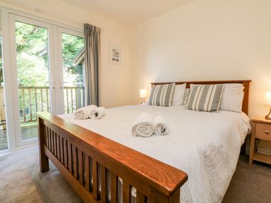 A bedroom with a wooden bed frame and striped pillows next to glass doors leading to a balcony at Stonewood Lodge in Woolsery