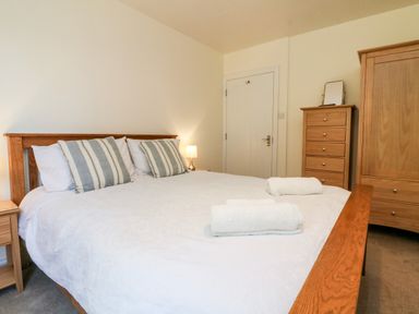 A bedroom with a double bed with pillows and towels a wooden wardrobe and chest of drawers at Stonewood Lodge in Woolsery