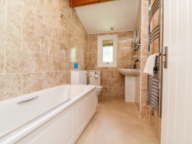 A bathroom with a bathtub a toilet a sink and a heated towel rail at Stonewood Lodge in Woolsery