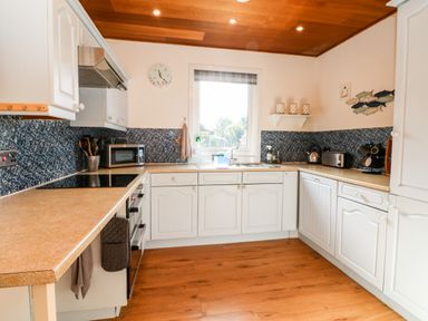 A kitchen with white cabinets brown countertops wooden floor and ceiling at Stonewood Lodge in Woolsery