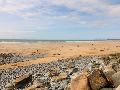 A sandy beach with scattered people and large rocks in the foreground at Stonewood Lodge in Woolsery