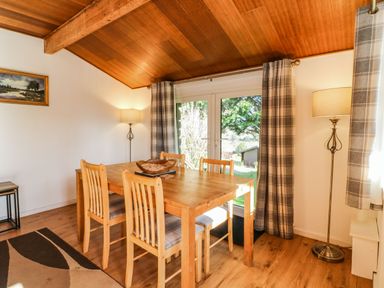 A dining area with a wooden table and four chairs next to large glass doors with plaid curtains at Stonewood Lodge in Woolsery