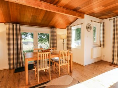 A dining area with a wooden table and four chairs near windows with plaid curtains at Stonewood Lodge in Woolsery