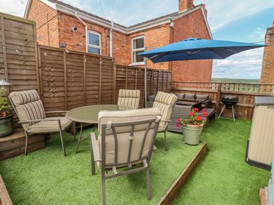 An outdoor patio area with chairs around a glass table a blue umbrella a grill and a sofa at Corner House in Cinderford