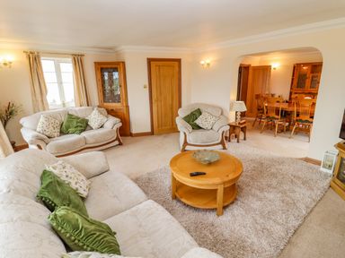 A living room with sofas and green cushions and a wooden coffee table leading to a dining area at Corner House in Cinderford