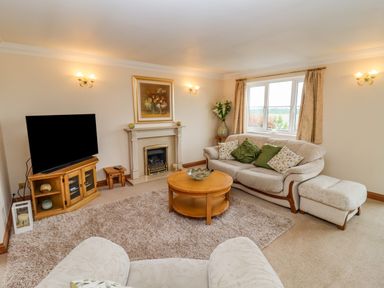 A living room with a sofa a television a fireplace and a round wooden coffee table at Corner House in Cinderford