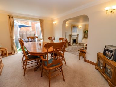 A dining room with a wooden table and chairs leading to a living room with a fireplace at Corner House in Cinderford