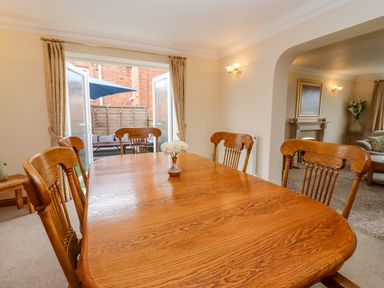 A dining room with a wooden table and chairs near open doors leading to a patio at Corner House in Cinderford
