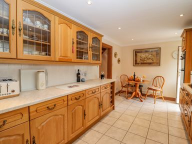 A kitchen with wooden cabinets a tiled floor a small dining table with chairs and wall art at Corner House in Cinderford