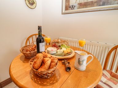 A wooden dining table with baskets of bread, a bottle of wine, glasses of orange juice, cheese and grapes at Corner House in Cinderford