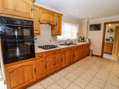 A kitchen with wooden cabinets a built-in oven a gas stove a sink a coffee maker and a television on the wall at Corner House in Cinderford