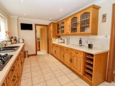 A kitchen with wooden cabinets a sink a gas stove and a wall-mounted television at Corner House in Cinderford
