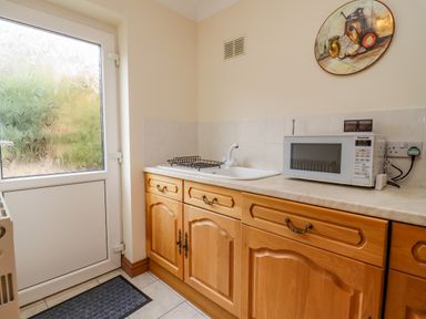 A kitchen with wooden cabinets a microwave and a sink next to a frosted glass door at Corner House in Cinderford