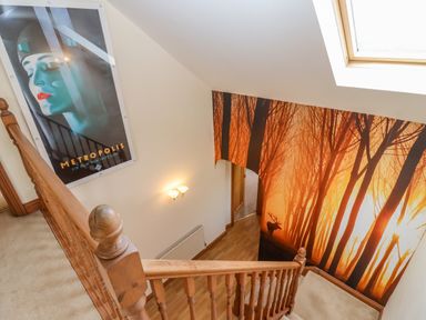 A staircase with wooden handrails and a wall poster of a forest with a deer at Corner House in Cinderford